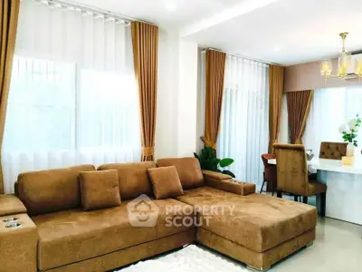 Elegant living room with plush brown sofa and dining area, featuring modern decor and ample natural light.
