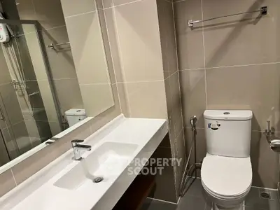 Modern bathroom with sleek fixtures and neutral tiles, featuring a spacious sink and contemporary toilet.