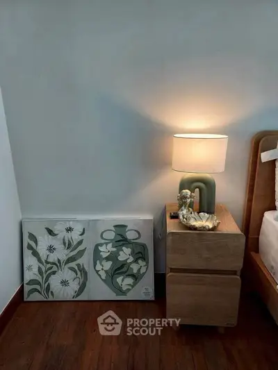 Stylish bedroom corner with modern lamp and artistic decor on wooden nightstand.