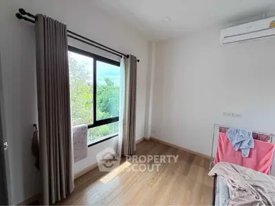 Bright bedroom with large window and air conditioning, featuring wooden flooring and modern curtains.