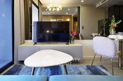 Modern living room with stylish decor and large TV, featuring elegant furniture and vibrant accents.