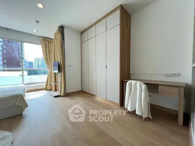 Spacious bedroom with wooden flooring and built-in wardrobe, featuring a city view from the window.