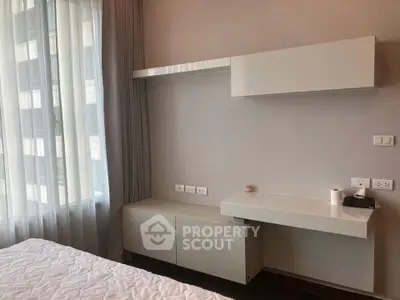 Modern bedroom with sleek built-in desk and storage, large window with curtains, and neutral decor.