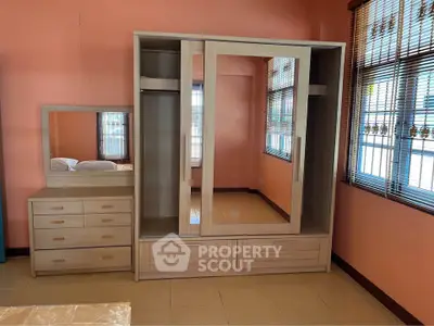 Spacious bedroom with modern wardrobe and dresser, featuring large windows and ample natural light.