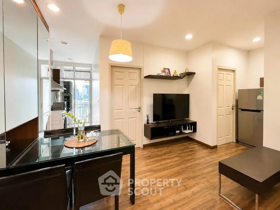 Modern living room with dining area and kitchen, featuring sleek furniture and wooden flooring.