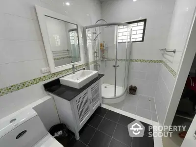 Modern bathroom with sleek black floor tiles, white cabinetry, and a curved glass shower enclosure complemented by green mosaic accents.