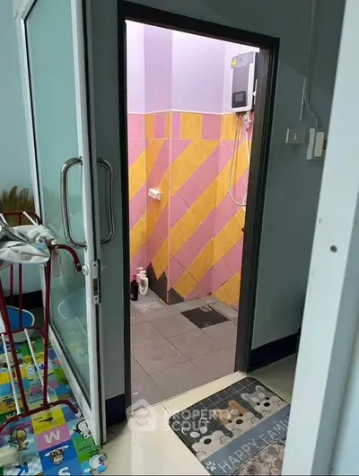 Colorful bathroom with pink and yellow tiles, visible shower area, and playful floor mat.