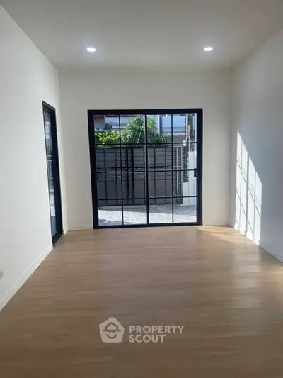 Bright empty room with large sliding glass doors and wooden flooring, perfect for customization.