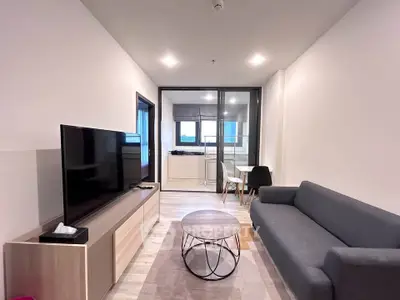 Modern living room with sleek furniture and large TV, open layout leading to dining area.