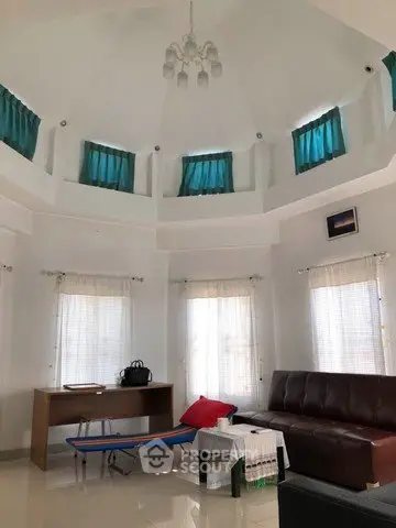 Spacious living room with high ceiling and modern decor, featuring large windows and elegant lighting.