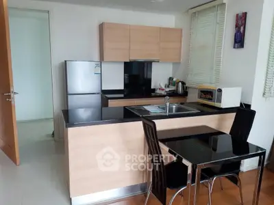 Modern kitchen with sleek cabinetry, black countertops, and dining area in a stylish apartment.