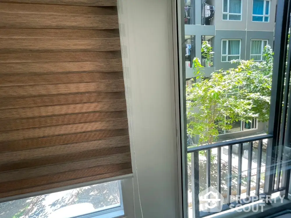 Modern apartment window view with stylish blinds and lush greenery outside.