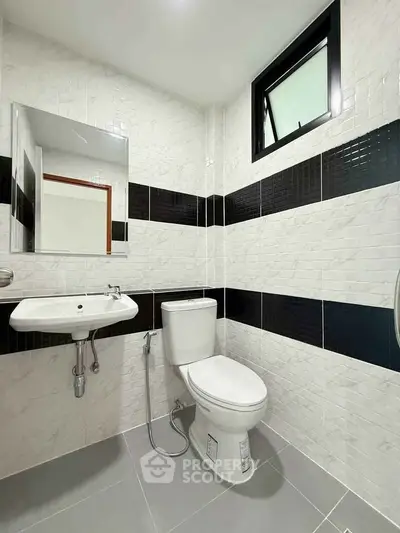 Modern bathroom with sleek white and black tile design, featuring a toilet and sink.