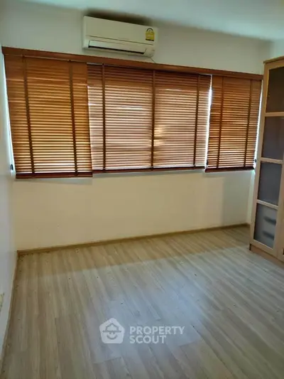 Spacious room with wooden flooring and large windows with blinds, ideal for customization.