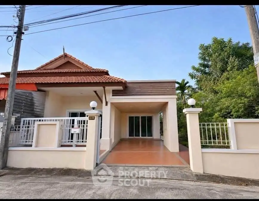 Charming single-story house with tiled roof and spacious driveway, surrounded by lush greenery.