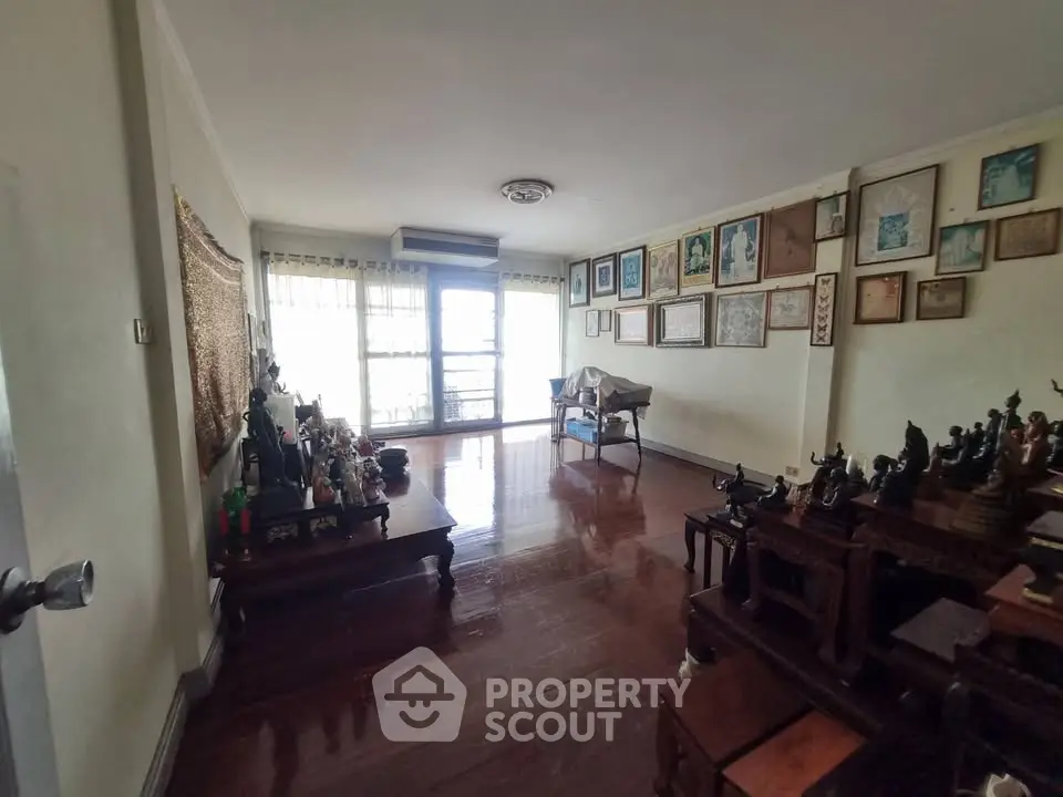 Spacious living room with wooden flooring and abundant natural light, featuring unique decor and art pieces.