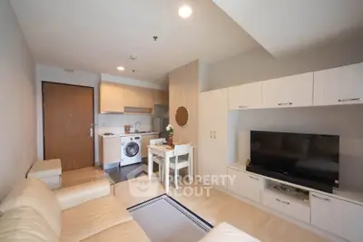 Modern living room with open kitchen, featuring sleek cabinetry and cozy seating area.