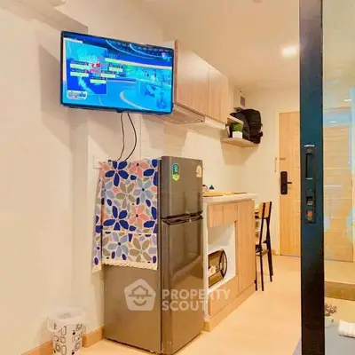 Modern kitchen with compact fridge and wall-mounted TV in cozy apartment.