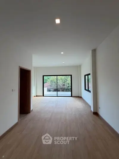 Spacious modern living room with large windows and wooden flooring, offering a serene view.
