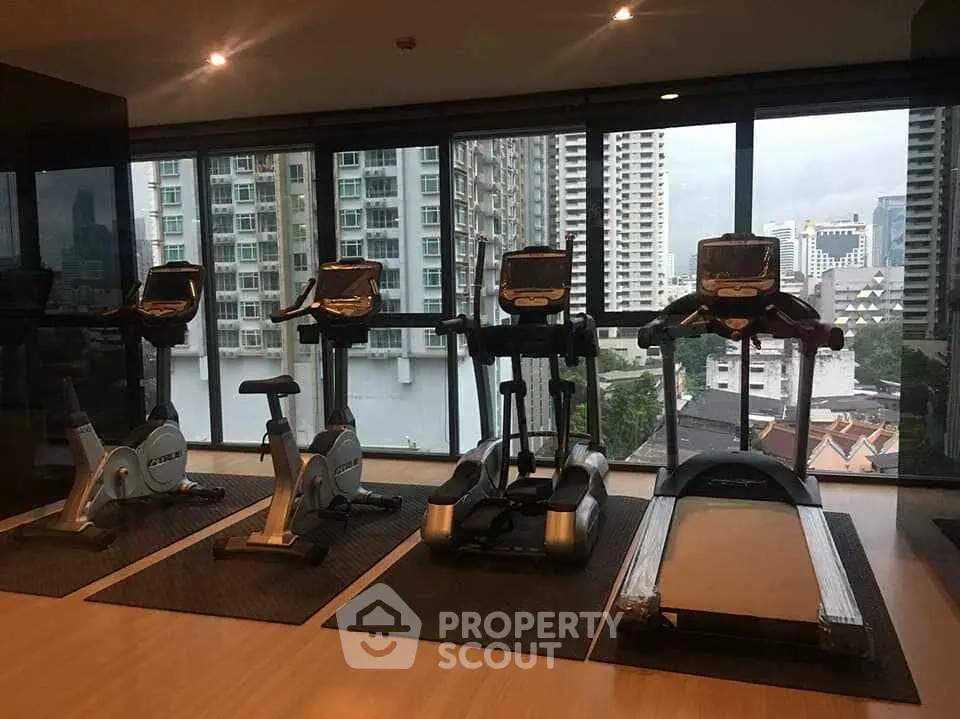 Modern gym with city view featuring treadmills and exercise bikes in a high-rise building.