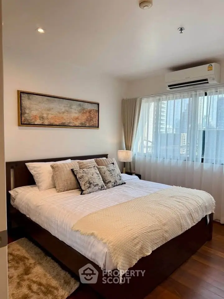 Cozy bedroom with modern decor and city view, featuring a comfortable bed and stylish artwork.
