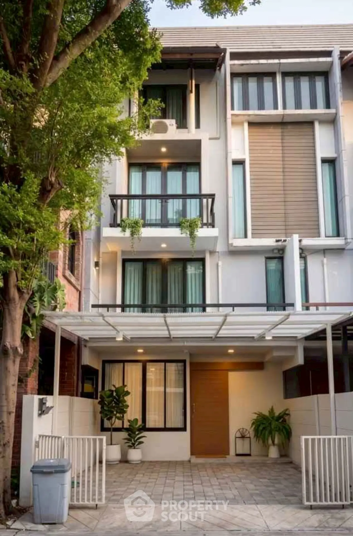 Modern three-story townhouse with sleek facade and lush greenery in urban setting.