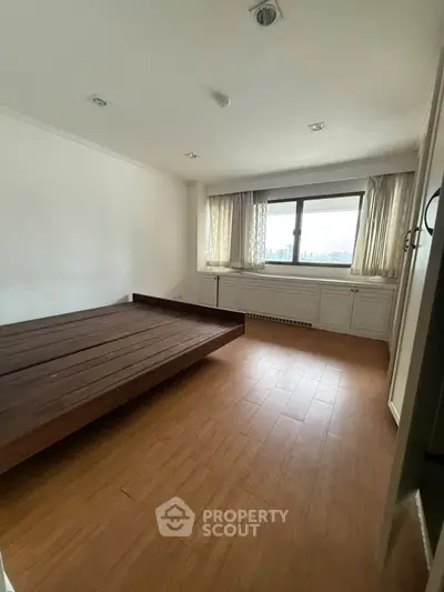 Spacious bedroom with wooden flooring and large window offering city views.