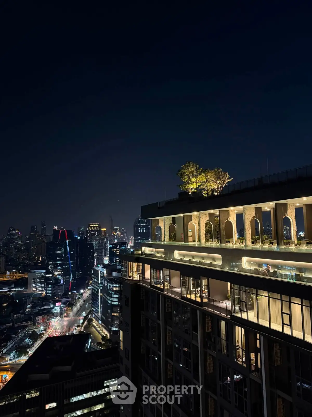 Stunning night view of a modern high-rise building with illuminated rooftop garden and city skyline.
