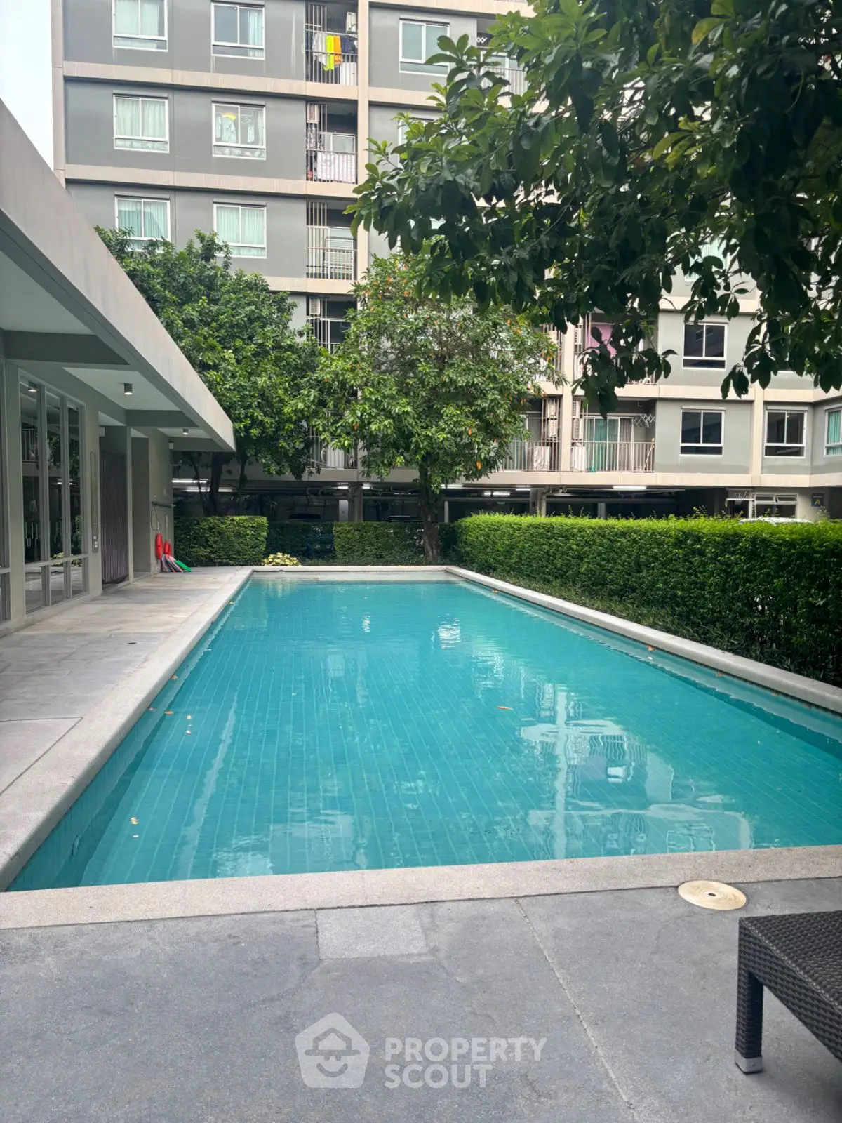 Modern apartment complex with a pristine swimming pool surrounded by lush greenery.