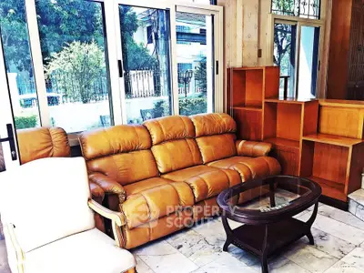 Spacious living room with leather sofa and large windows overlooking garden view.
