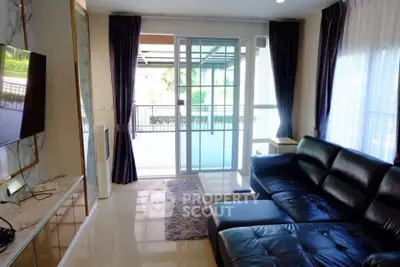 Modern living room with sleek black leather sofa and large windows leading to balcony.