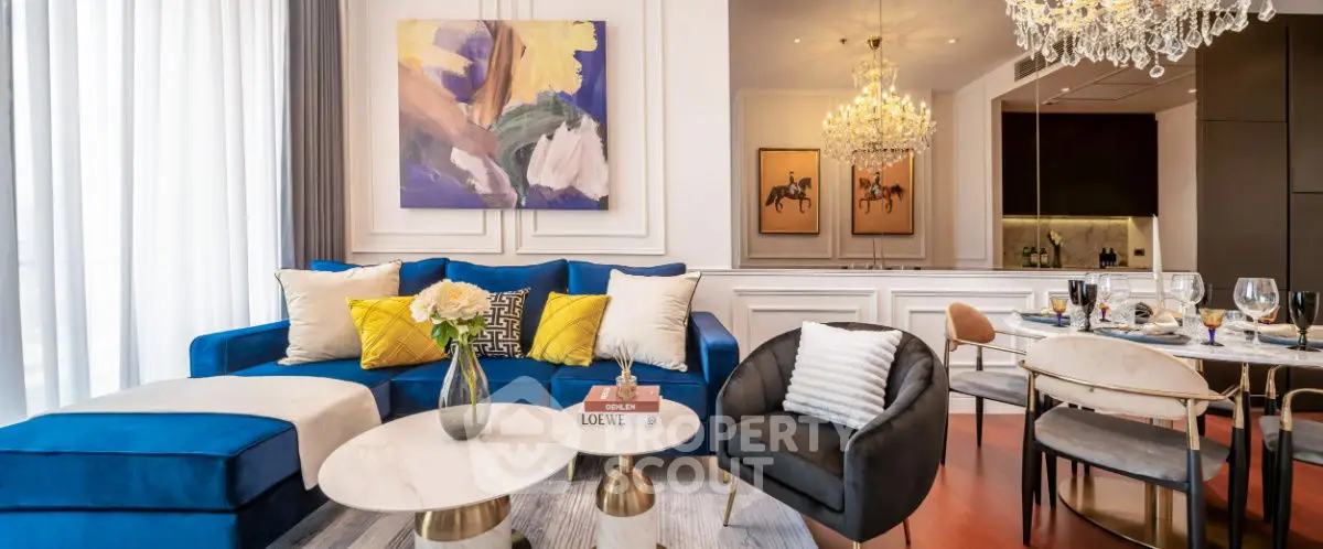 Luxurious living room with elegant decor, plush blue sofa, and modern dining area under chandeliers.