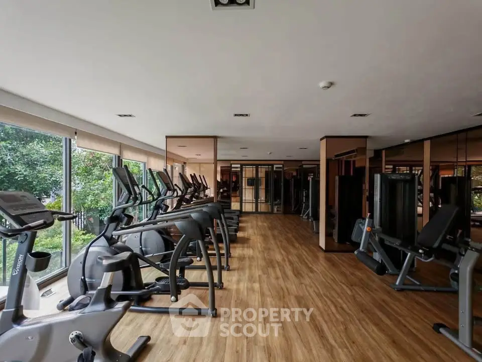 Spacious gym with modern equipment and large windows offering a serene garden view.