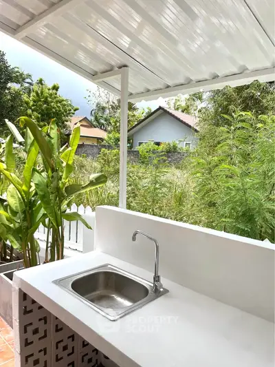 Charming outdoor kitchen with sink and lush garden view, perfect for alfresco dining.