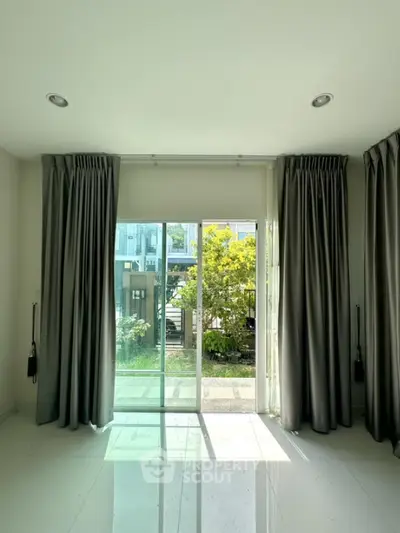 Bright room with large sliding glass doors opening to a lush garden view, featuring elegant curtains and glossy flooring.