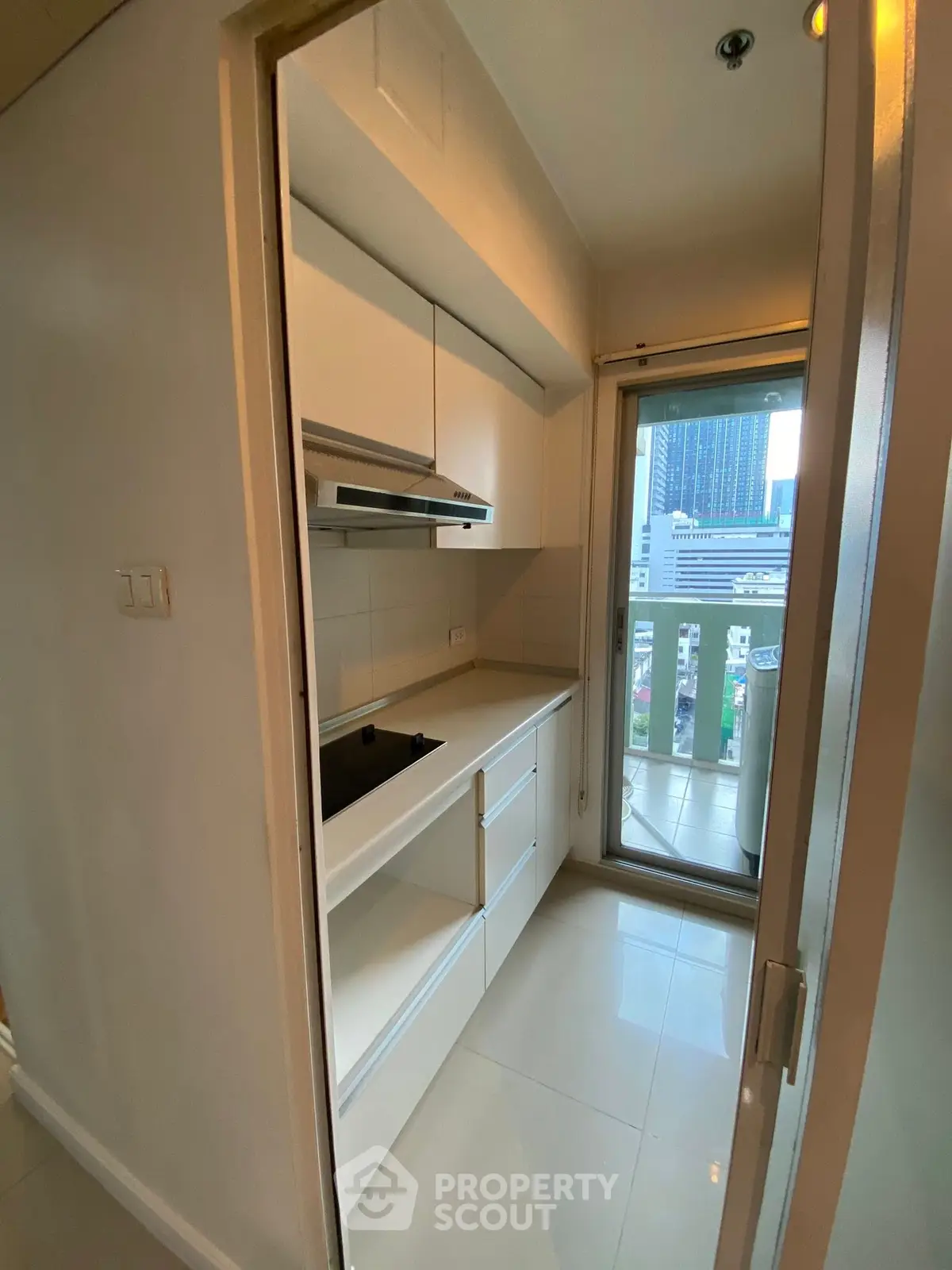 Modern compact kitchen with sleek white cabinets and city view balcony access.