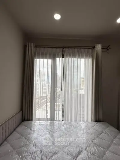 Cozy bedroom with large window offering city view, featuring a comfortable bed and elegant curtains.