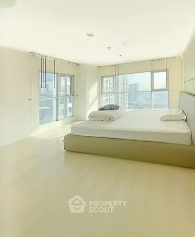 Spacious bedroom with large windows offering stunning city views in a modern apartment.