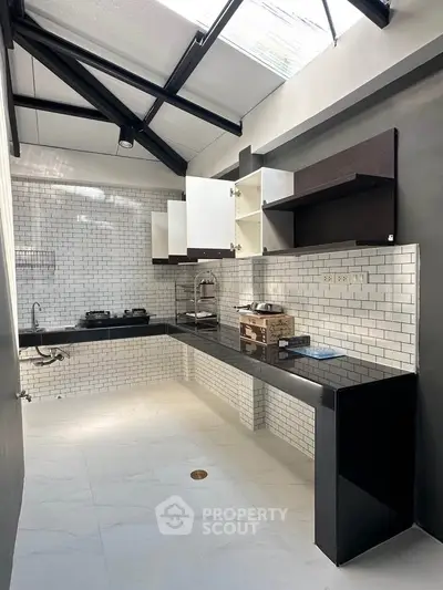 Modern kitchen with sleek black countertops and open shelving under a skylight.