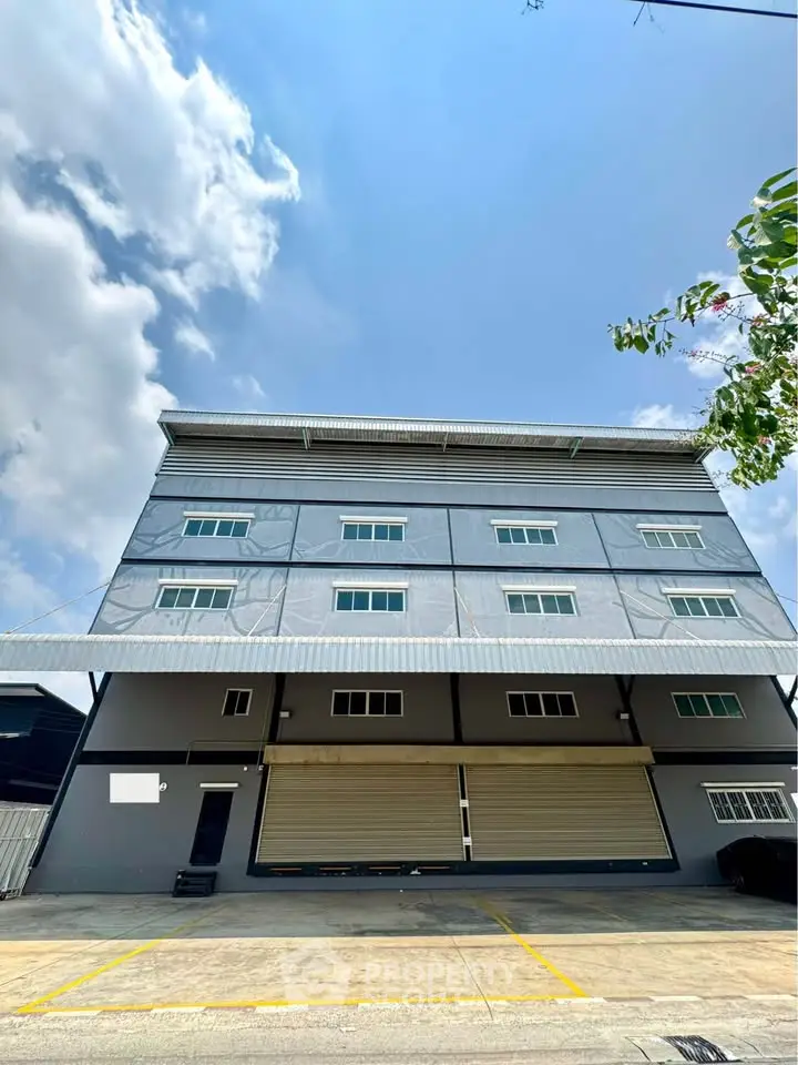 Modern industrial building with sleek design and ample parking space under a clear blue sky.