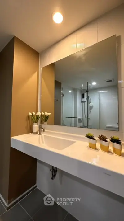 Modern bathroom with large mirror and elegant sink, featuring stylish decor and warm lighting.