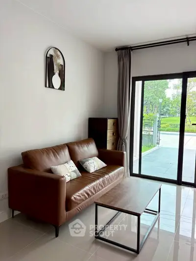 Modern living room with brown leather sofa and garden view through large window.