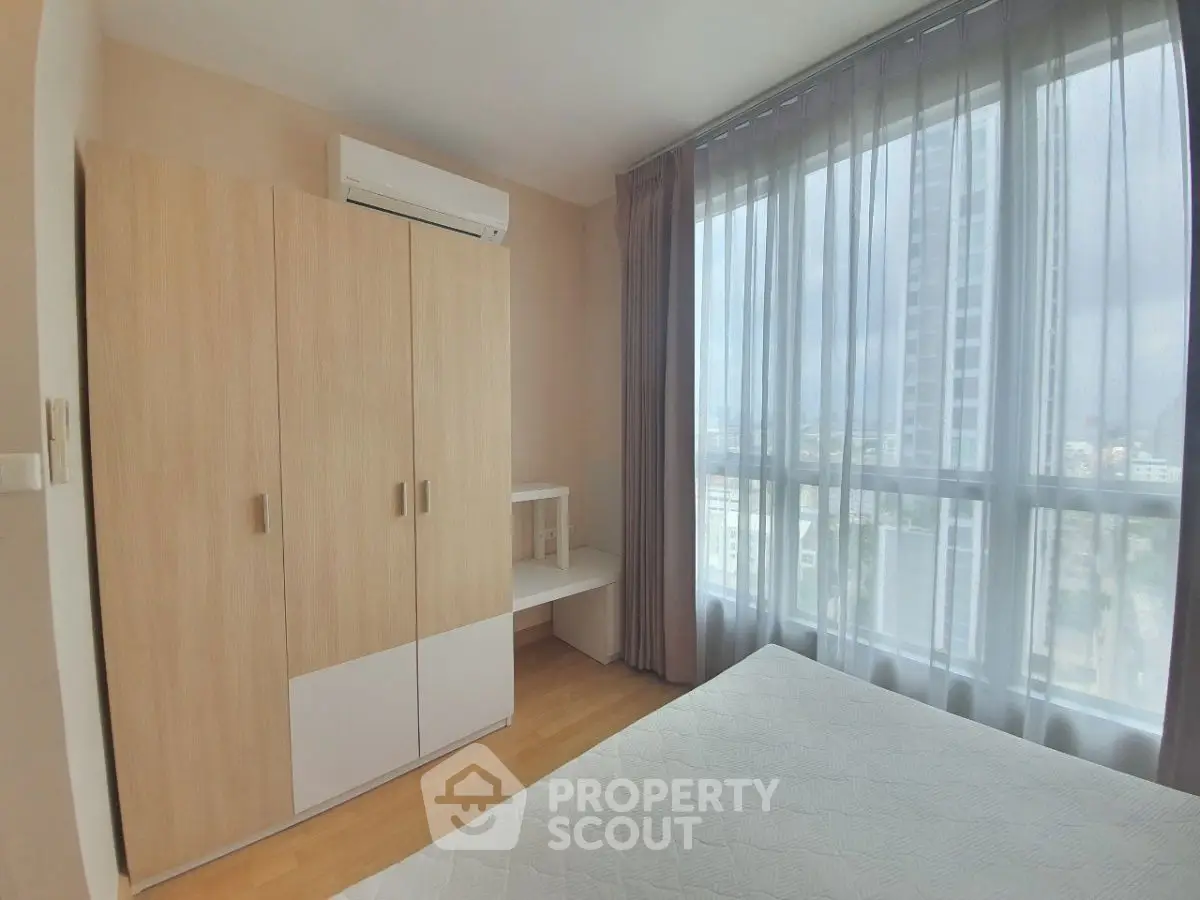 Bright bedroom with large window and modern furniture in a high-rise apartment.