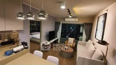 Modern living room with open kitchen and city view, featuring stylish lighting and cozy furnishings.