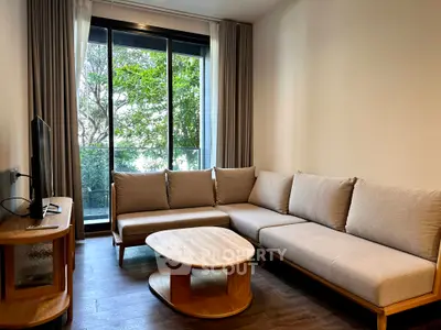 Modern living room with large windows and stylish furniture, offering a serene view of lush greenery.