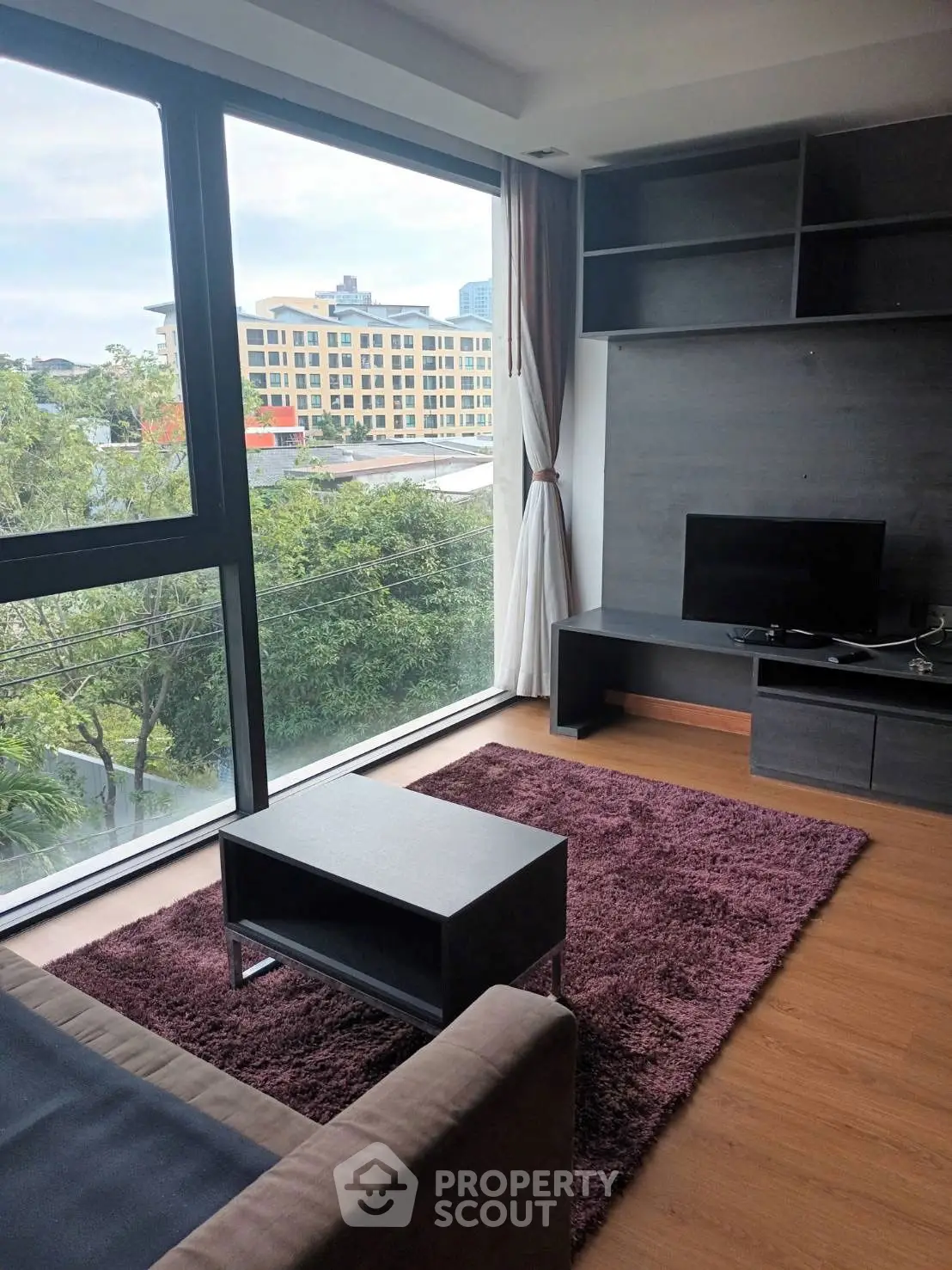Modern living room with large windows and city view, featuring sleek furniture and cozy rug.
