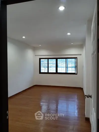 Spacious empty room with wooden flooring and large window, perfect for customization.