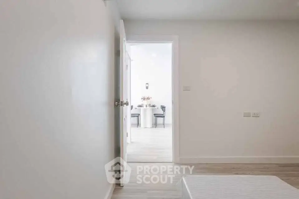 Minimalist interior with open door leading to bright dining area, showcasing modern design and spacious layout.