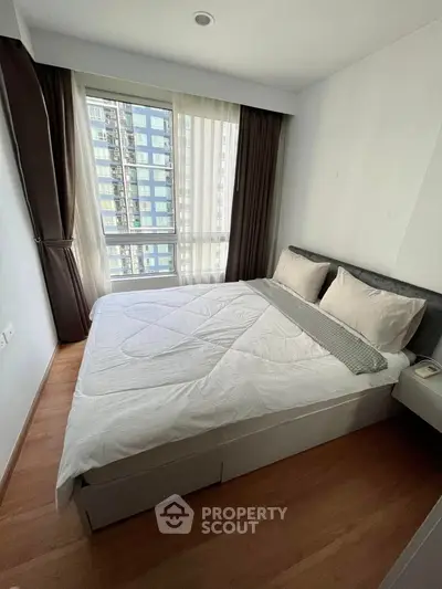 Modern bedroom with large window and stylish decor in urban apartment.
