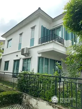 Modern two-story house with balcony and lush greenery